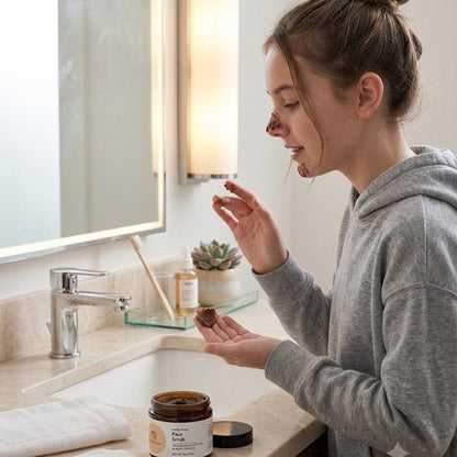 Woman applying facial scrub to her face in a bathroom.