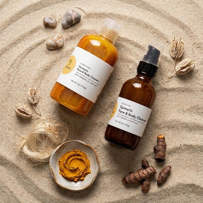 Two brown bottles with labels on a sandy surface with turmeric roots and a small dish of turmeric paste.